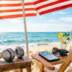 Ombrellone in spiaggia con smartphone e cuffie per ascolto di audiolibri e podcast in estate